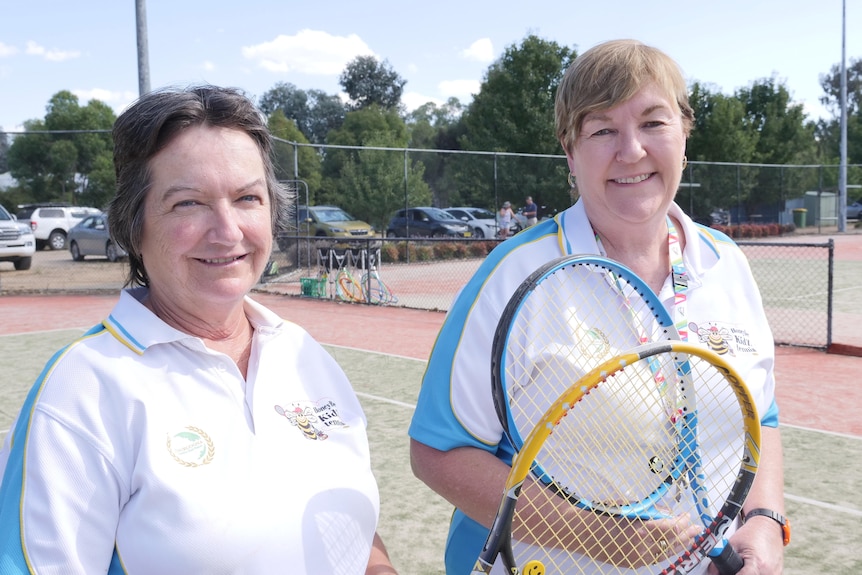 Two women standing on a tennis court holding a racquet in their hands 