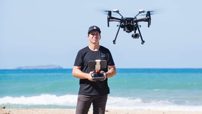 man on beach operating a drone with a handheld controller