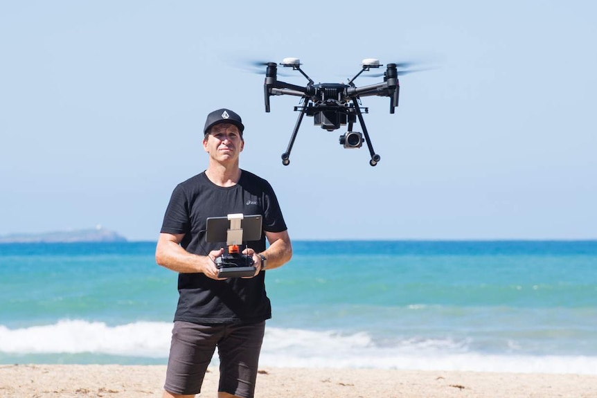 man on beach operating a drone with a handheld controller