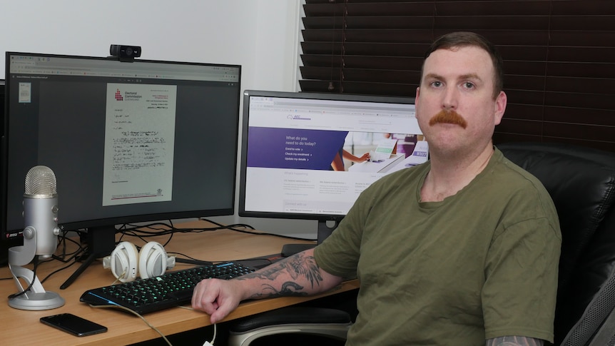 Man with a moustache sitting beside computer screen