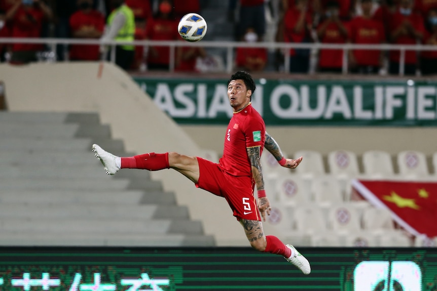 A Chinese football player captured mid-air with his legs spread and the ball above him 