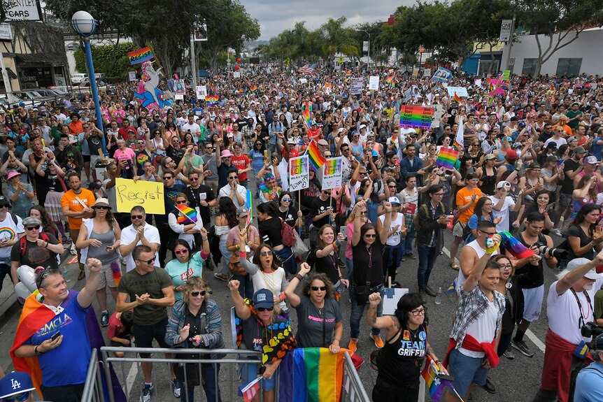 Hundreds of marchers holding rainbow flags and signs that say "resist" gather at the end of the Los Angeles LGBTQ march.