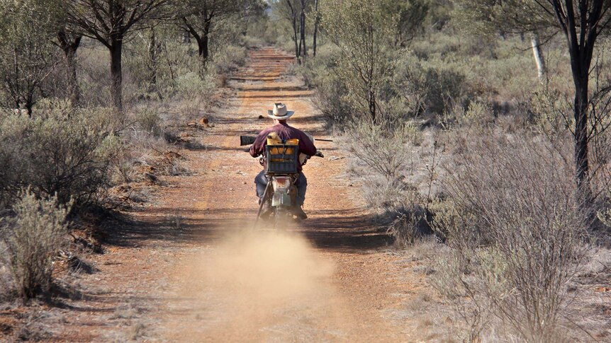 Don Sallway rides his motorbike down a dirt road on a property.