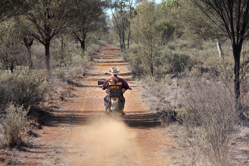 Don Sallway rides his motorbike down a dirt road on a property