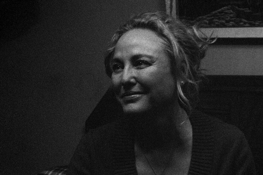 A black and white close-up still of Virginia Madsen smiling in the 2018 film 1985.