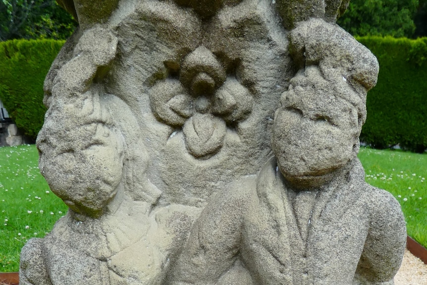 Image of sandstone sundial with male and female faces, eroded, and flower between.