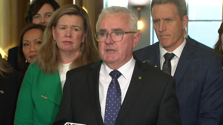 Politician speaks during a media conference flanked by other MPs.