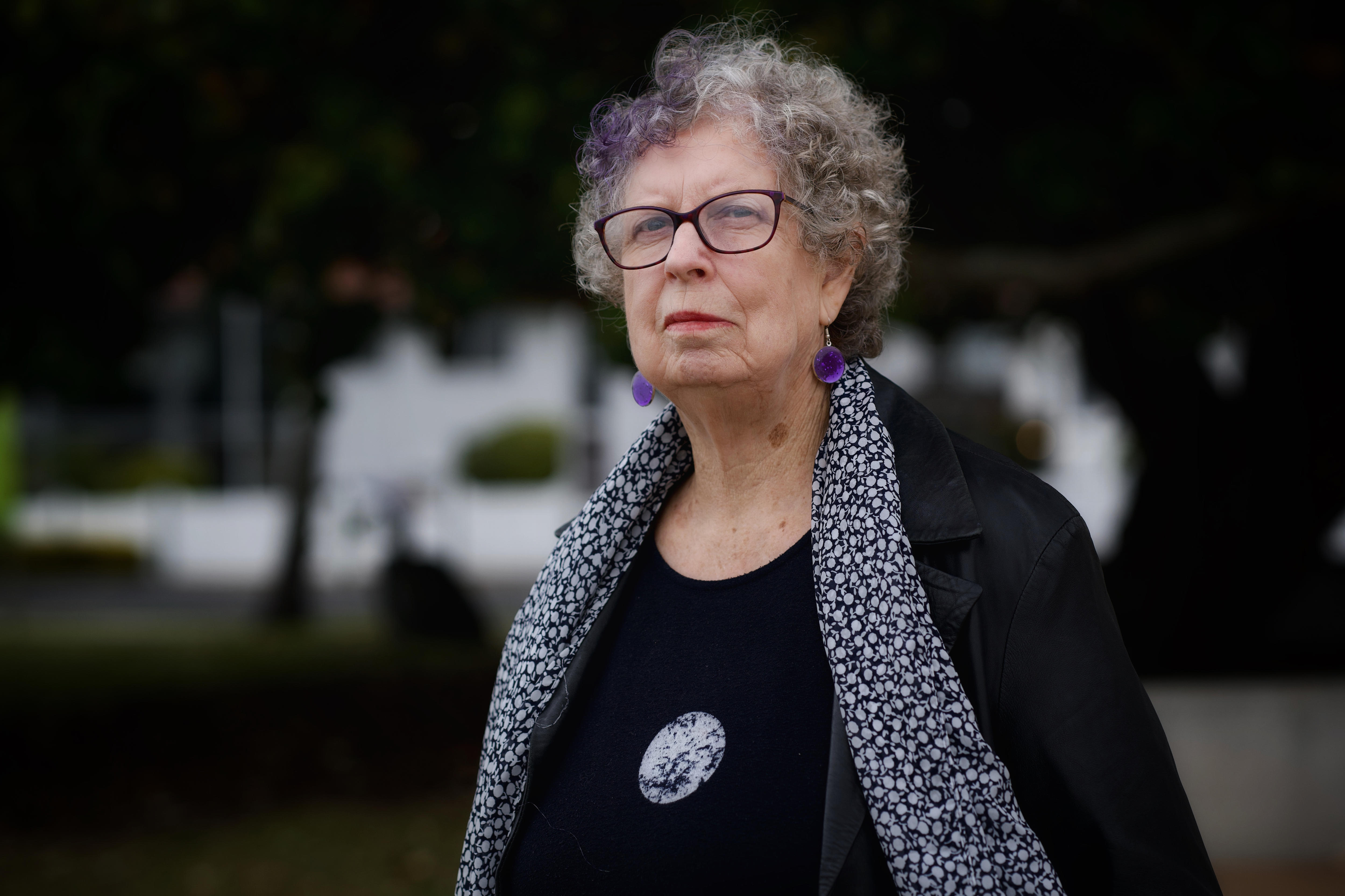 A woman wearing a black top with a scarf and black-framed glasses.