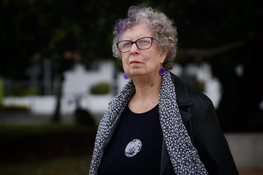 A woman wearing a black top with a scarf and black-framed glasses.