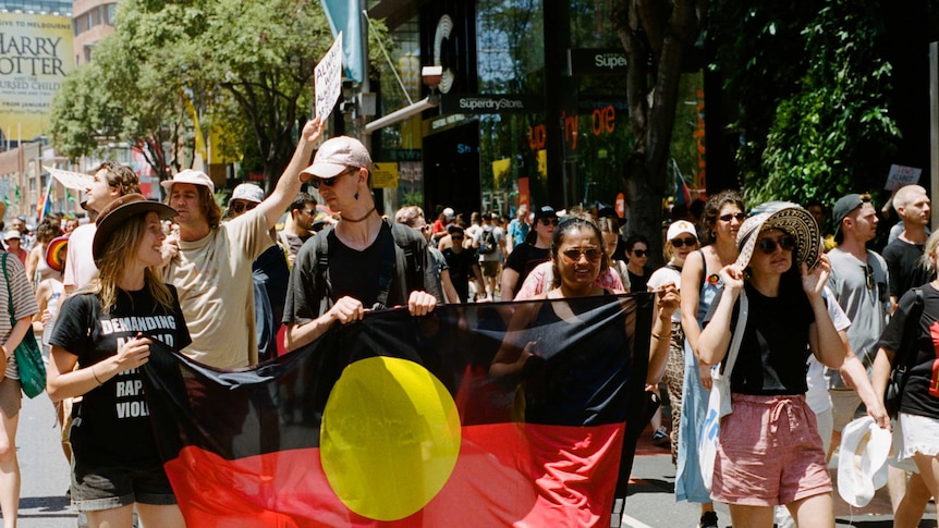 A group of marchers holds a large banner of the Aboriginal flag during the Yabun Festival, Sydney in 2019.