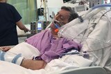 A man in a hospital bed with breathing tubes in his nose.