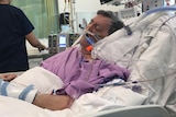 A man in a hospital bed with breathing tubes in his nose.