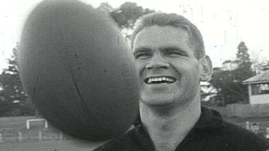 A young football player runs on the field in a striped guernsey.