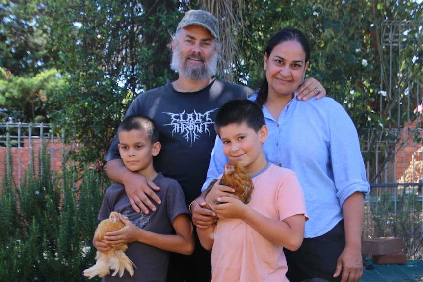 Craig and his wife and three children stand in a backyard, the kids hold chickens.
