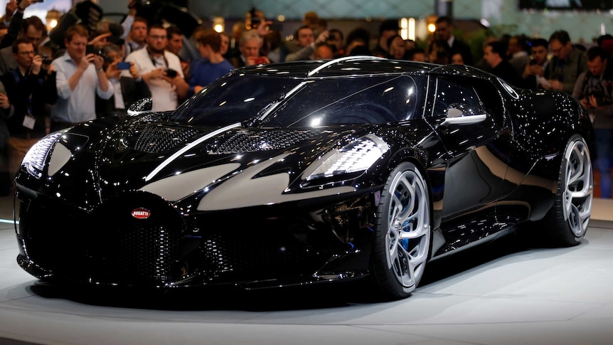 A glistening black Bugatti La Voiture Noire at a motor show.