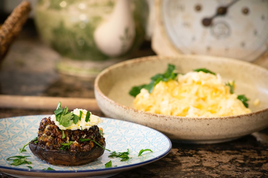 Two plates of food, one featuring a stuffed mushroom and one with scrambled eggs