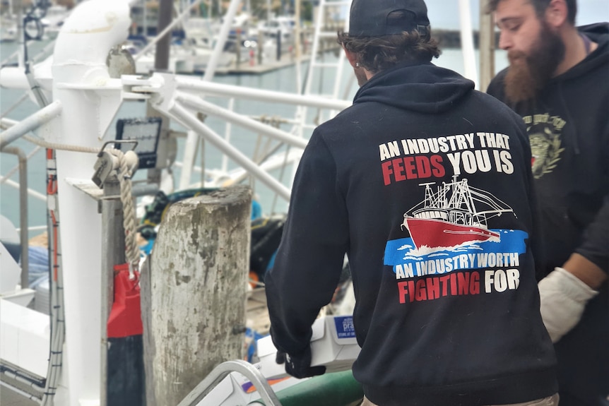 Two men carry boxes on a dock.