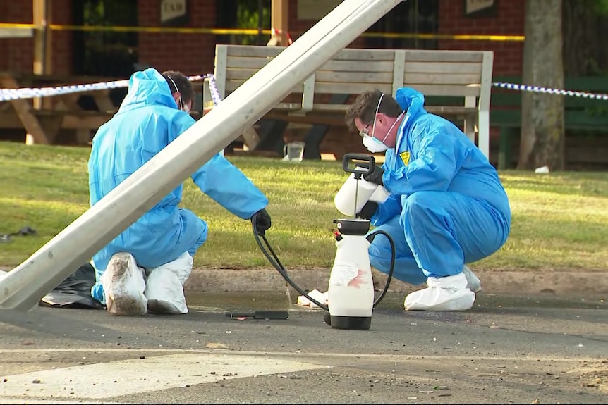 Investigators in blue hazmat suits comb through debris on a road.