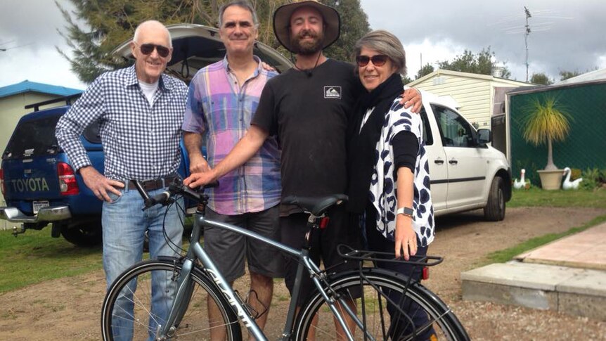 Chris Anderson stands with his arm around a woman and alongside two men with a new mountain bike.
