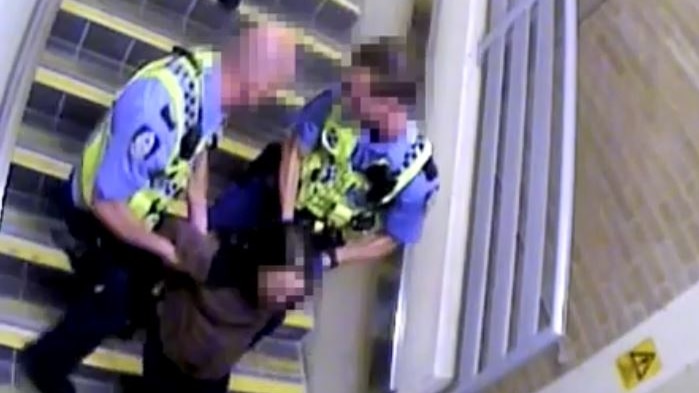 Two police officers hold a woman arms behind her back as they attempt to drag her up a flight of stairs.