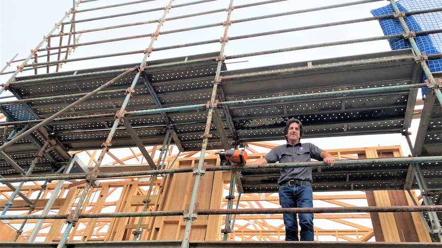 A man holding a building tool standing on scaffolding. 