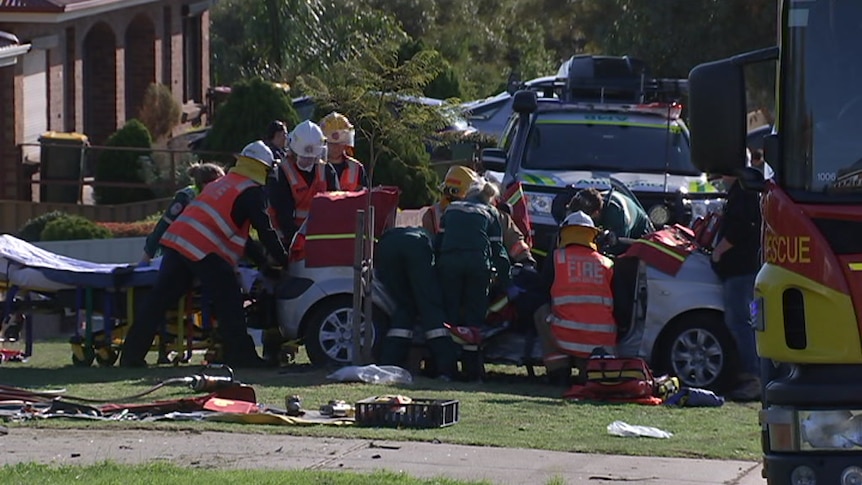 A hatchback surrounded by emergency services personnel on a footpath