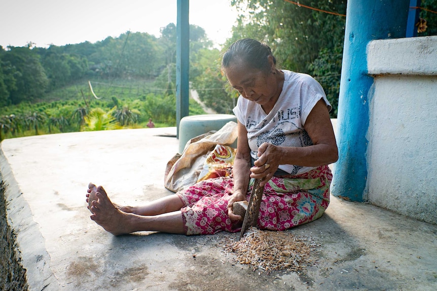 An Indonesian woman sitting on a balcony grates a cassava root