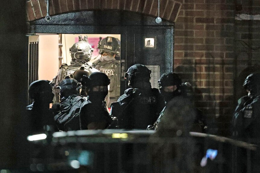 A swat team enters a brick building at night.