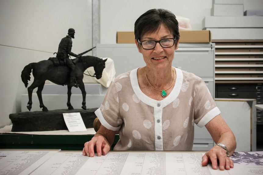 A woman with short brown hair and glasses sits at a desk.