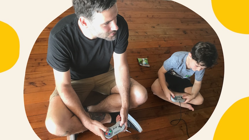 A man and a boy sit on the floor with computer game controllers