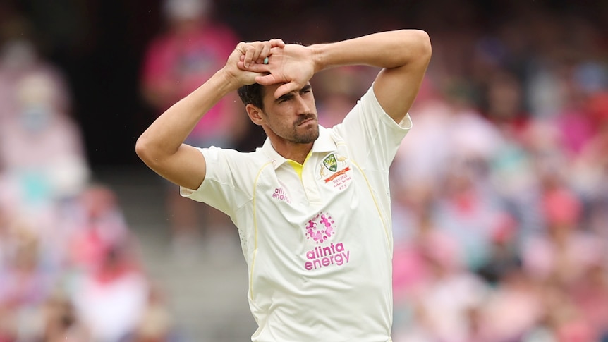 Mitchell Starc holds both his hands on the top of his head with his elbows out either side