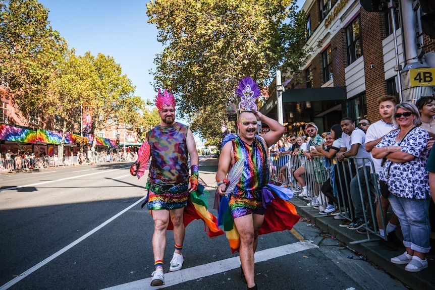 two men dressed up in glittery outfits walking along a street