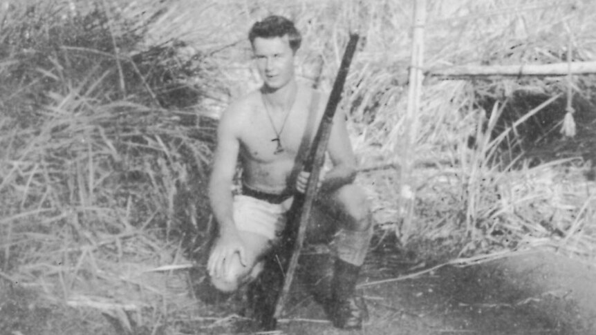 Black and white photo of a man crouching, holding a machine gun.