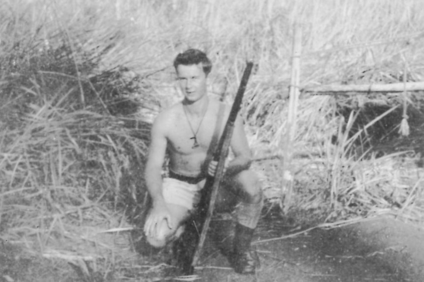 Black and white photo of a man crouching, holding a machine gun.