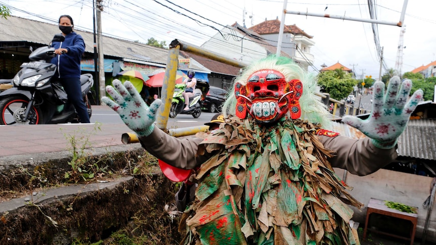 A police officer wearing a Balinese traditional mask, called celuluk, performs to warn people about coronavirus.