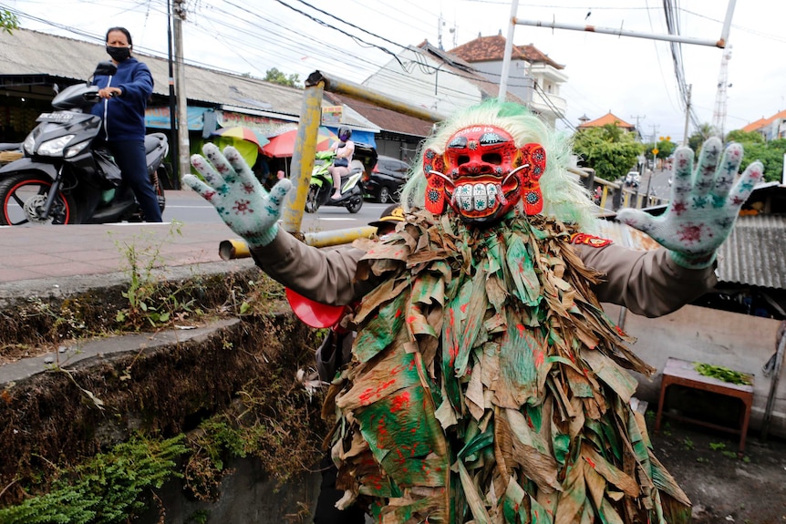 A police officer wearing a Balinese traditional mask, called celuluk, performs to warn people about coronavirus.