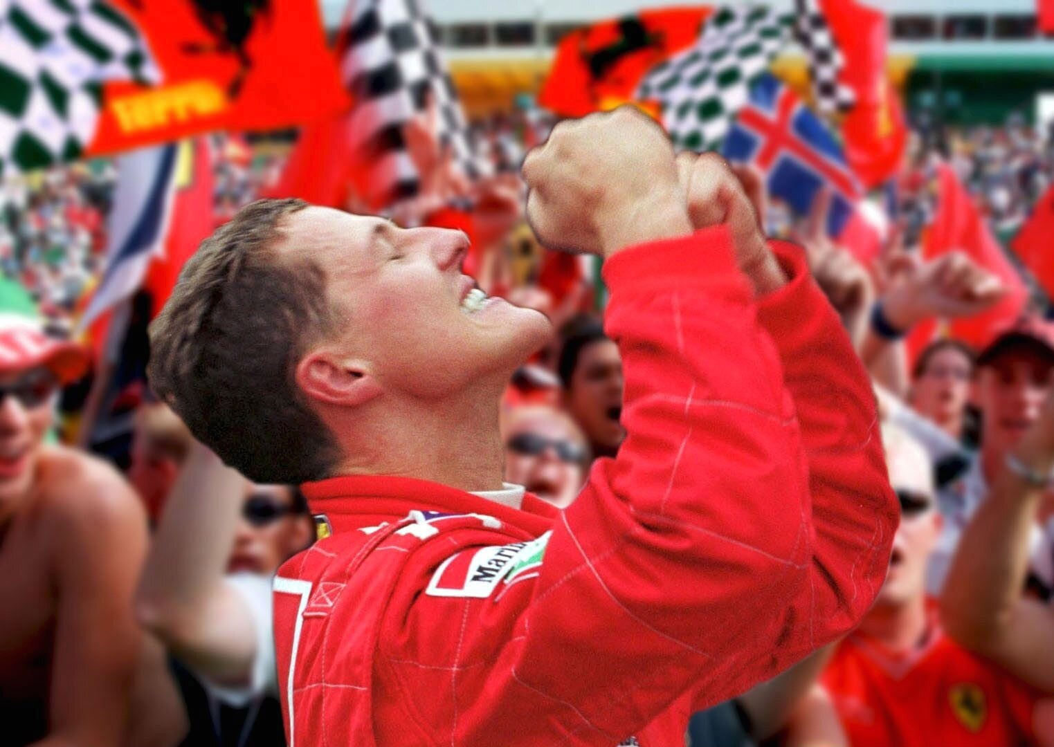 A racing driver in a red racing suit, looking to the sky, pumping his fists, in front of cheers fans