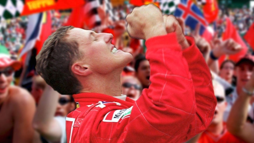 A racing driver in a red racing suit, looking to the sky, pumping his fists, in front of cheers fans