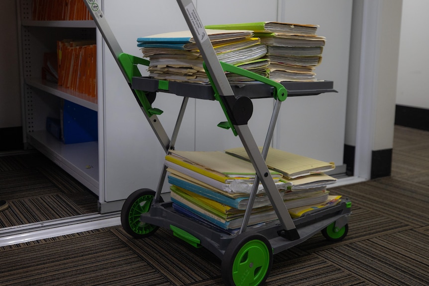 A metal trolley in a corridor stacked with manila folders and files 