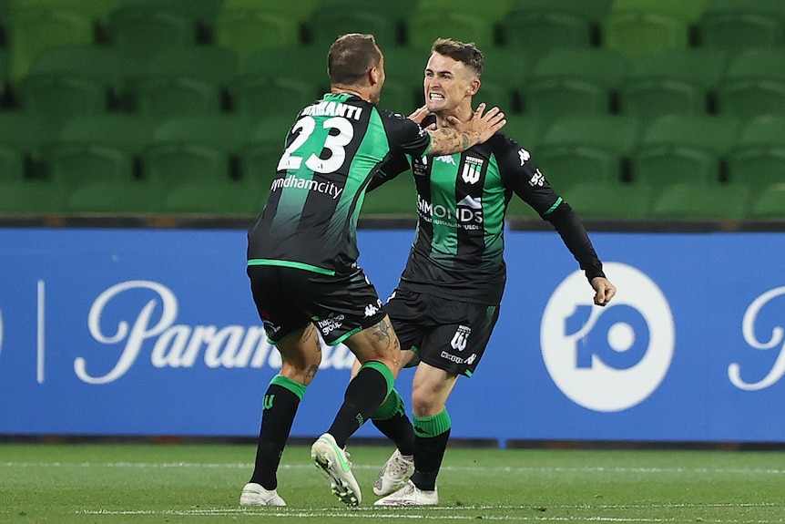 Two soccer players hug after a goal.