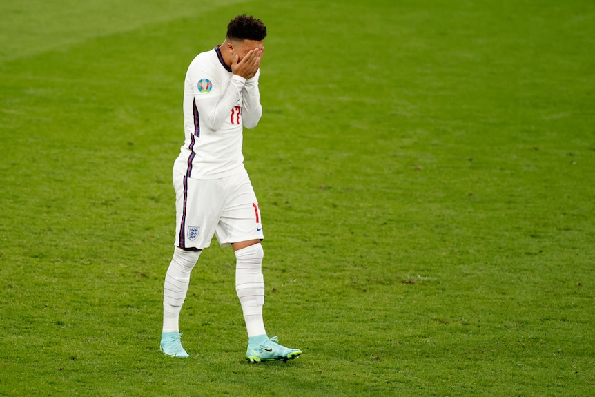 Jadon Sancho walks with his hands covering his face