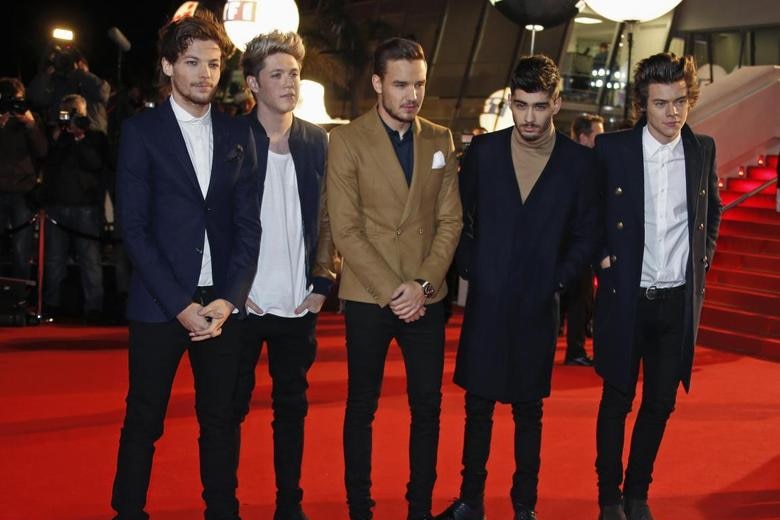 Five men dressed in formal suits stand on a red carpet