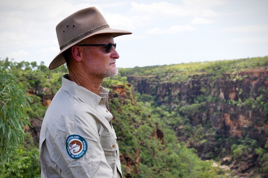 A man in a hat and park ranger's uniform stares out over a large gorge