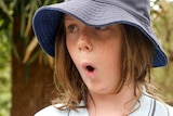 Boy with shoulder length brown hair in blue hat with lips pursed