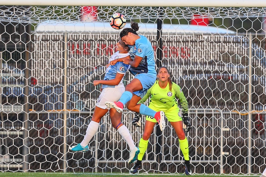 Sam Kerr leaps high into the air as she wins an aerial contest against another defender directly in front of goal.