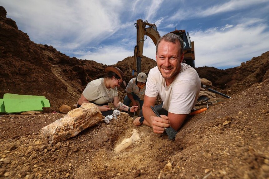 Man smiles at camera next to newly-discovered fossil