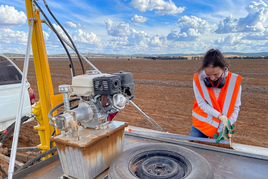 Woman standing next to drill rig inspecting soil sample in crop field. 