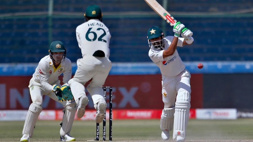 Pakistan batter Babar Azam hits a cricket ball, forcing Australia fielder Travis Head to jump out of the way.