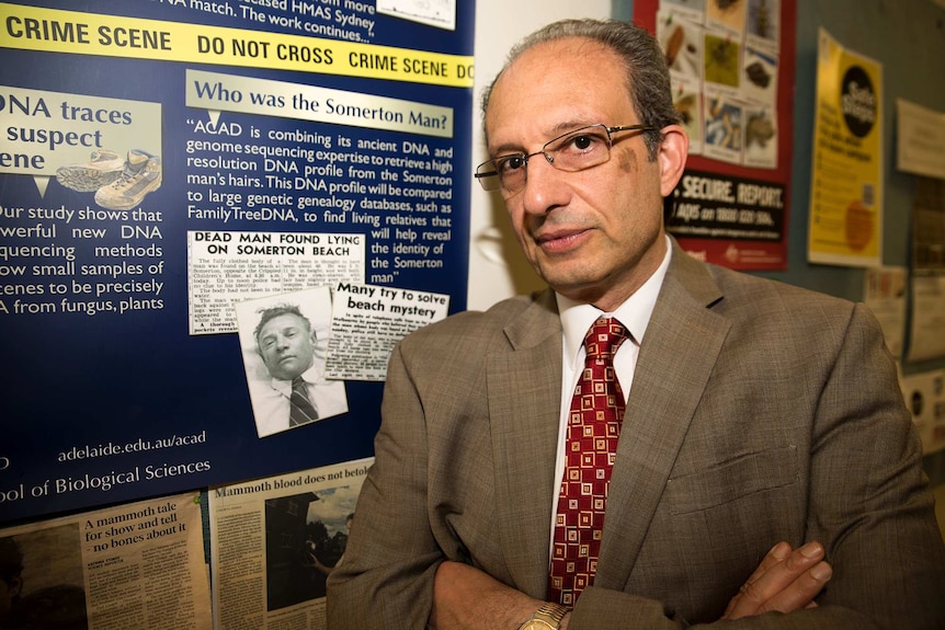 Derek Abbott stands next to a wall with photos of the Somerton Man