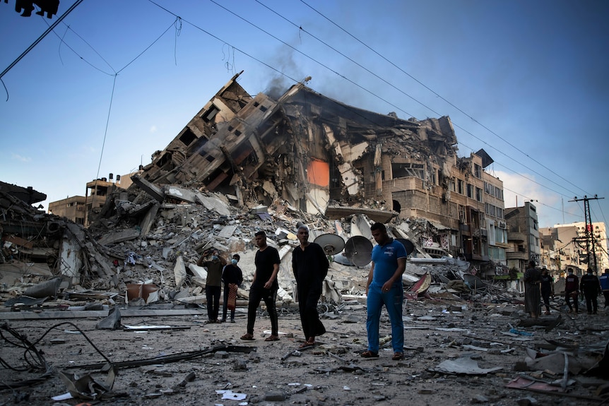 A group of men walk next to the ruins of a large building in Gaza